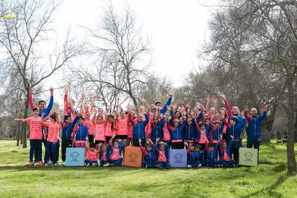 Grupo de niños y adultos en un parque, vestidos con ropa deportiva rosa y azul y con los brazos levantados.