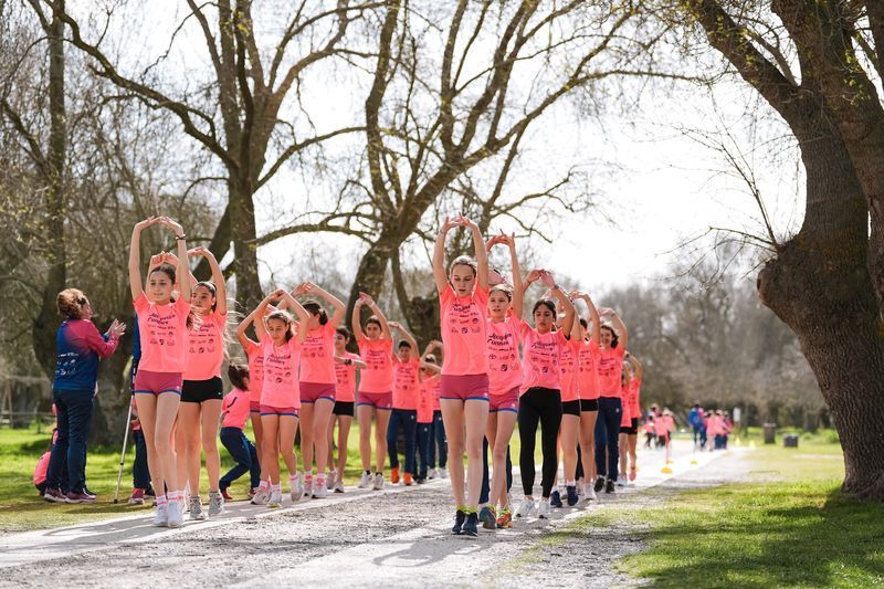Las jóvenes con camisetas rosas se estiran al aire libre, con los brazos en alto.