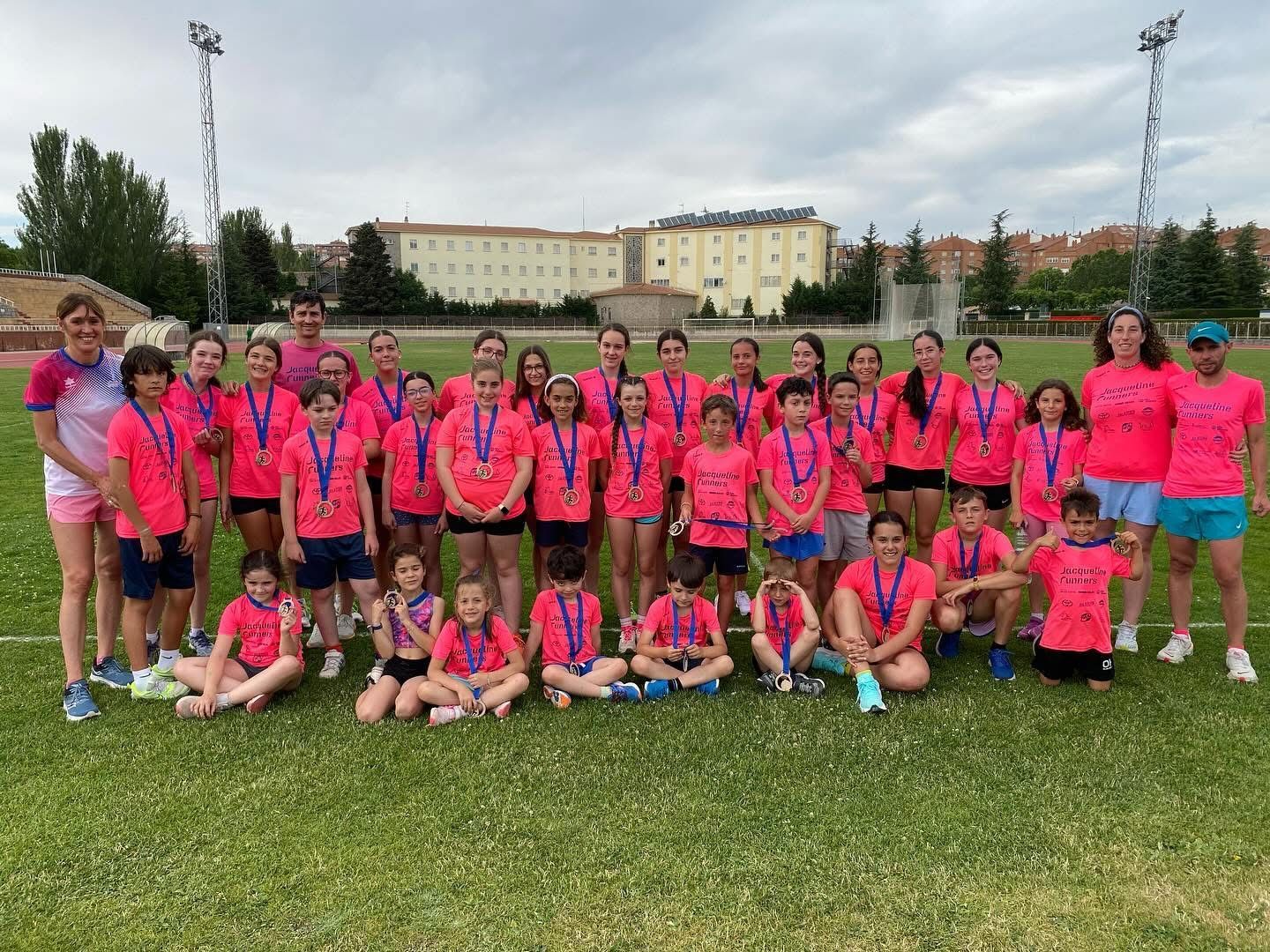 Grupo de jóvenes atletas con camisetas rosas y medallas en un campo verde.